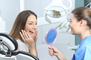 woman in a dentist chair smiling looking at her Invisalign 