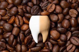 Big fake tooth on coffee beans showing teh declaration teeth suffer and why teeth whitening. 
